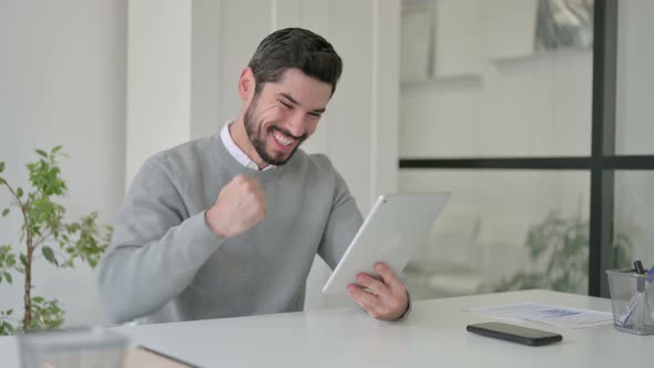 Young Man Celebrating Success on Tablet in Office