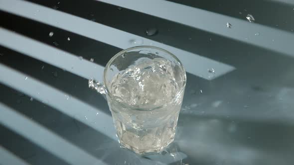 Two Pieces of Crushed Ice Falls Into Transparent Glass with Clean Drinking Water on Blue Background
