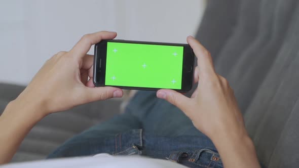 Woman at Home Lying on a Couch Using with Green Screen Smartphone in Horizontal Landscape Mode