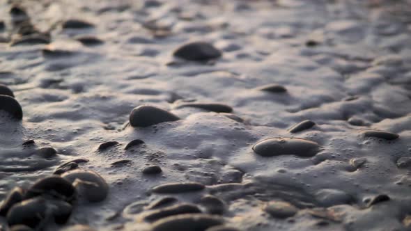 Close up beach waves and water streaming through pebbles and rocks slowmo