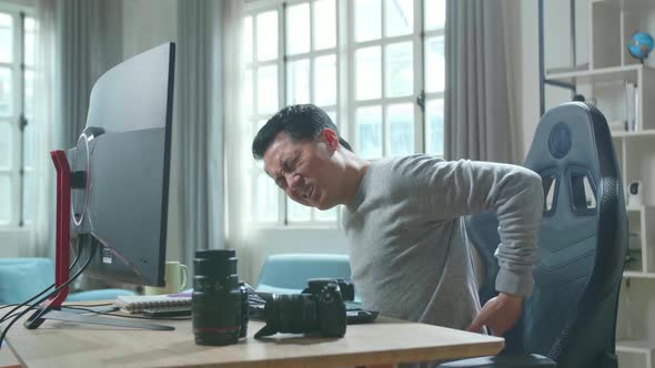 Asian Cameraman Having Backache While Using Desktop Computer For Working At Home