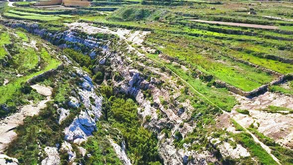 Arial shot rising up out of the rocky valley of Wied Il-Ghasri for a birds eye view of the grassy pl