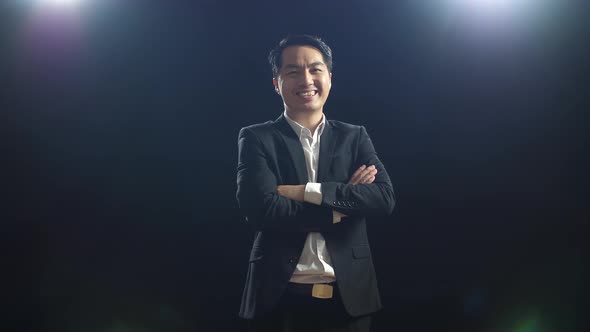 Asian Speaker Man In Business Suit Crossing His Arms While Standing In The Black Screen Studio