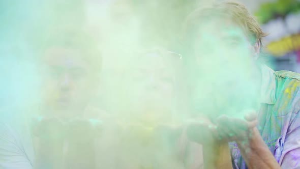 Cheerful Young Men and Woman Blowing Colorful Powder to Camera at Holi Festival