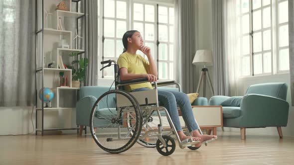 Asian Kid Girl Sitting In A Wheelchair And Thinking Then Raising Her Index Finger In Living Room