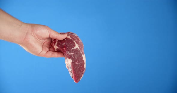 A Man's Hand Holds a Steak Raw Beef Ribeye. 