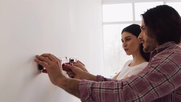 Young Couple Using Waterpas for Measuring Wall Level Making Home Renovation Together