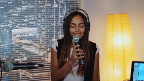 Beautiful Multiracial Girl in Headphone Singing Into Microphone and Recording a Song in Home Studio