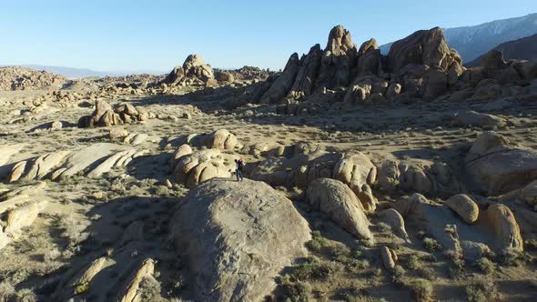 Aerial shot of a young man backpacker standing on a boulder with his dog in a desert mountain range.