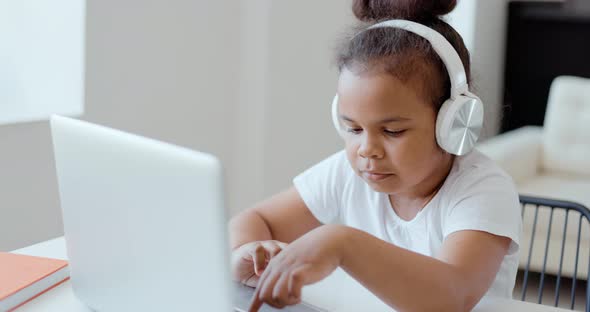 Afro American Kid Girl School Pupil Wearing Headphones Studying Online From Home Watching Web Class