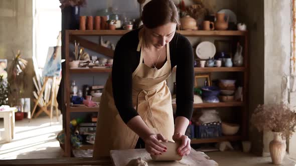 Front View of Female Potter Wearing Beige Apron Kneading Softly Clay Piece on Worktop Working with