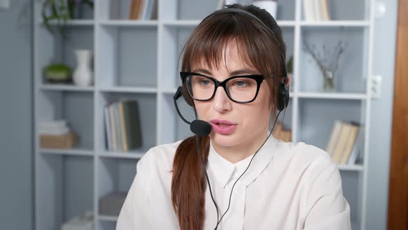 Business woman in headphones with a microphone talking with a client using a laptop