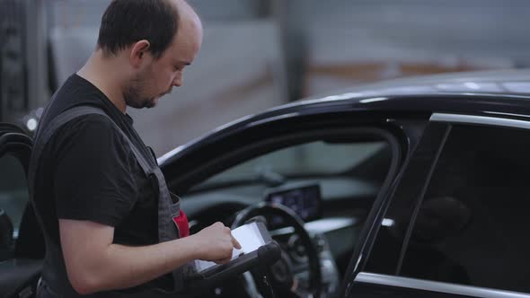 Portrait A Mechanic in a Car Service Closeup Holds a Tablet in His Hands and Presses on the Screen