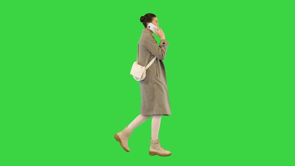 Young Woman in Stylish Clothes Walks Talking on Mobile Phone on a Green Screen Chroma Key