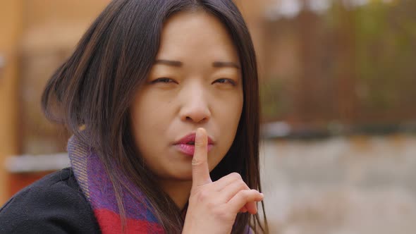 attractive asian woman makes silence gesture with finger- outdoor
