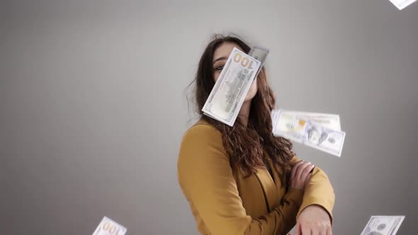 Young Woman in Yellow Costume is Posing on White Background Among Flying Cash in Air in Slowmo