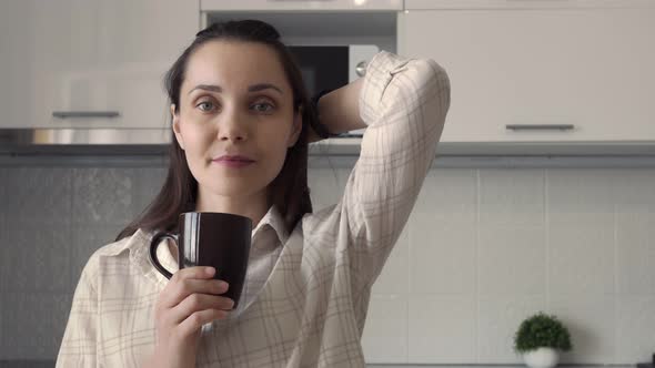 A Young Darkhaired Woman with Bushy Hair Stands in the Kitchen