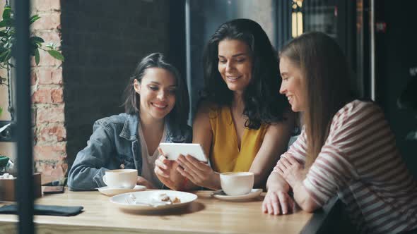 Group of Young Women Watching Smartphone Screen Laughing Drinking Coffee in Cafe