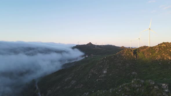 Wind turbines spinning on mountain at sunrise and clouds on valley, Caramulo in Portugal. Aerial for