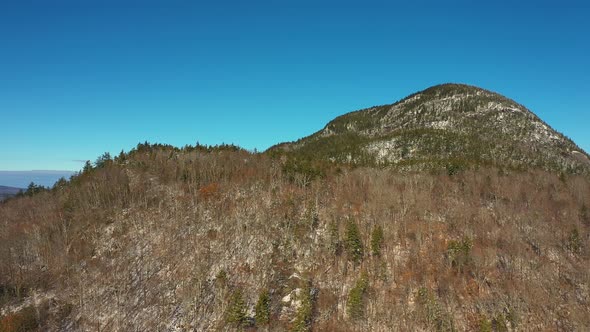 Aerial footage rising orbit around a forested mountain after late fall snow