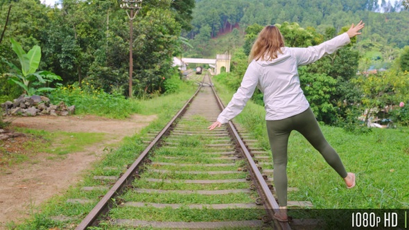 Woman Balancing on Train Track Rail with Lush Green Forest in the Background