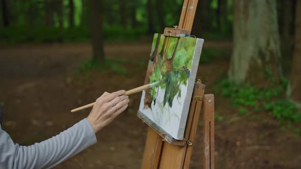 Side View of a Girl's Hand Painting a Landscape on Canvas in a Park