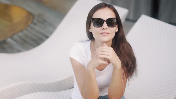 Brunette Girl Wearing Sunglasses Smiles on Couch at Resort