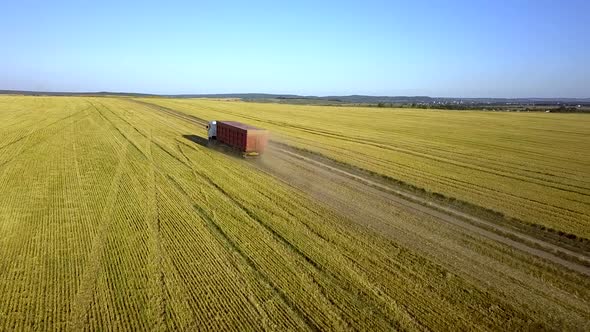 Aerial view of a truck driving on dirt road between plowed fields making lot of dust.