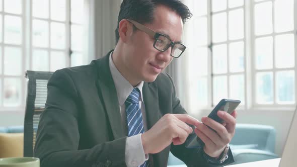 Asian Businessman Using Mobile Phone While Using The Computer For Working At Home