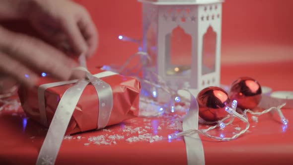 Wrapping Christmas gift with ribbon and red paper with red background and baubles