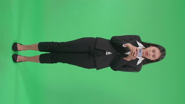 Full Body Of Asian Business Woman Thinking While Using Mobile Phone In The Green Screen Studio