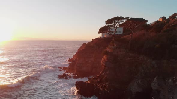 Aerial: waves hitting rocks near a modern house, revealed, then the town of Sestri Levante in Italy