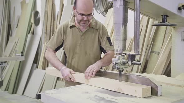 Diligent woodworker cutting lumber using trimming machine in workroom