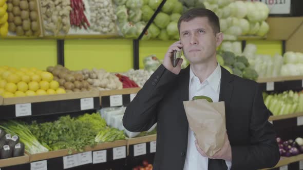 Young Serious Caucasian Man Hanging Up the Phone in Grocery and Sighing. Confident Businessman in
