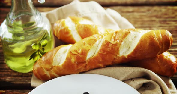 Olive oil, bread loaf and pickled olives on table