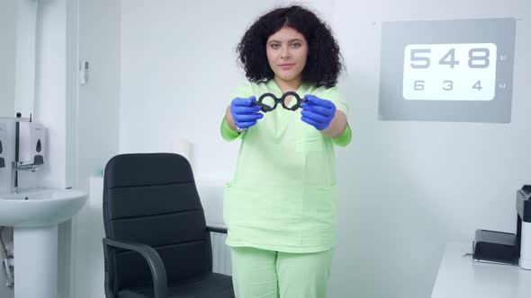 Medium Shot of Smiling Ophthalmologist Stretching Trial Lens Frame Standing in Hospital Indoors