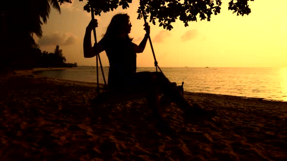 Girl Is Swinging on the Swings at the Ocean Shore While the Sun Goes Down.