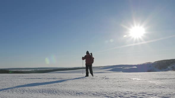 A Man with Backpack and Trekking Sticks Against the Backdrop of Winter Mountains, Beautiful Sunset