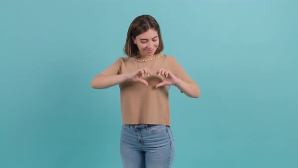 Happy Woman Put Make with Fingers Heart Shape, Isolated on Turquoise Background.