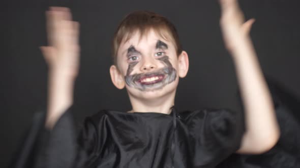 Caucasian cheerful boy 8 years old in black clothes and with a monster make-up on his face looks at 