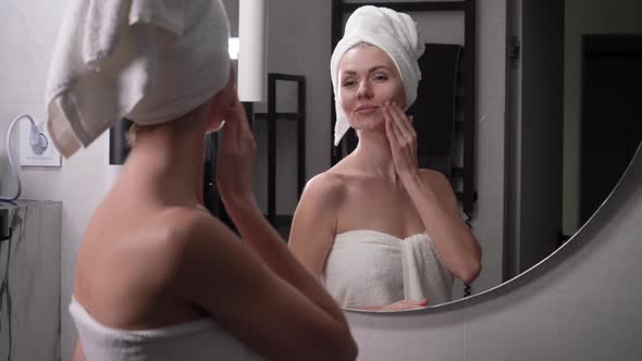 Happy Attractive Young Woman with a Towel on Her Head Touching Her Face Applies Cream