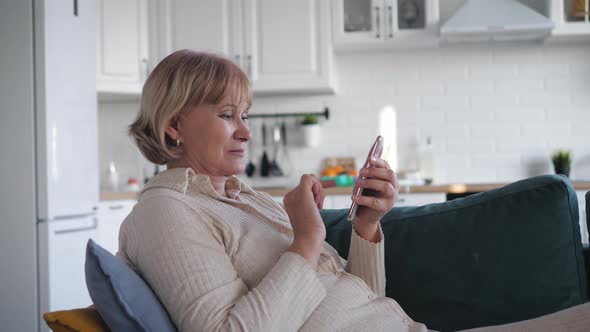 Housewife In Living Room Lying On Couch Uses Smartphone