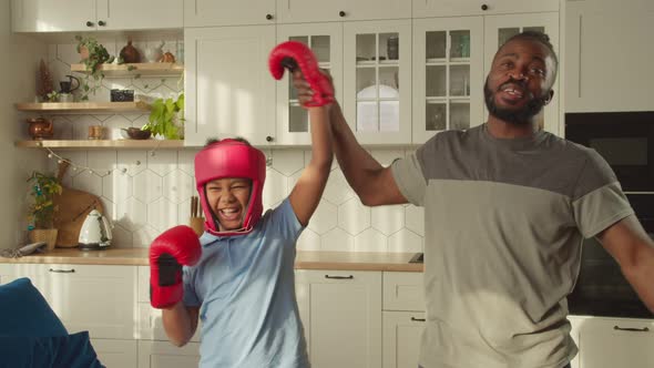 Proud African Father Raising Up Hand of Little Son in Boxing Gloves As Winner