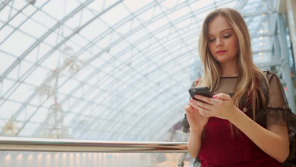 Happy Teenage Girl Holding Bags with Purchases, Smiling While Looking at Phone in Shopping Center