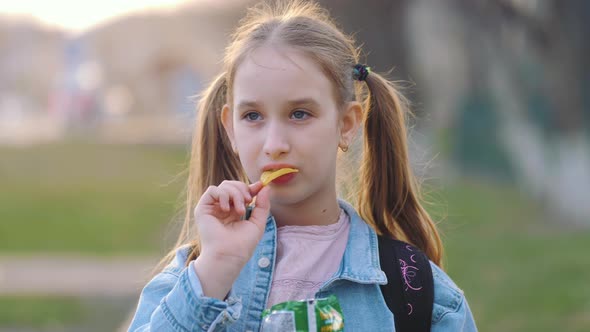 Young School Girl Eating Chips From Packet on Street