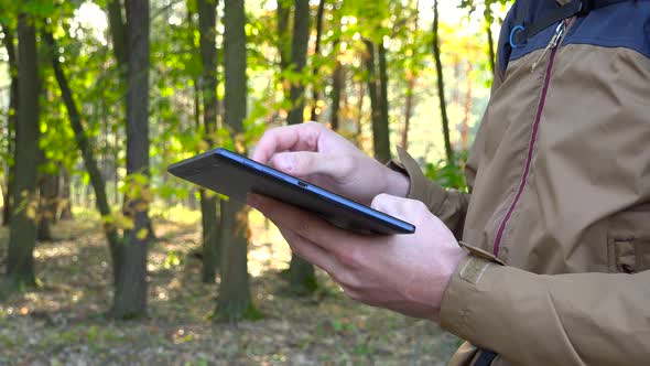 A Backpacker Works on a Tablet in a Forest - Closeup From the Side