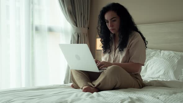 Beautiful European Young Serious Woman Freelancer Working on a Laptop Sitting on a Bedroom at Home