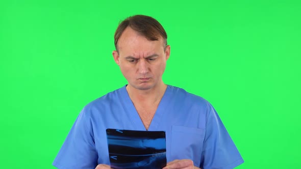 Male Doctor in Blue Coat Reviewing X-ray Pointing on Snapshot. Green Screen