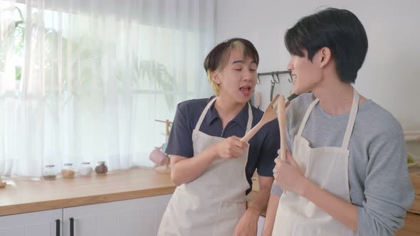 Asian happy handsome man gay couple sing and dance together while cooking foods in kitchen in house