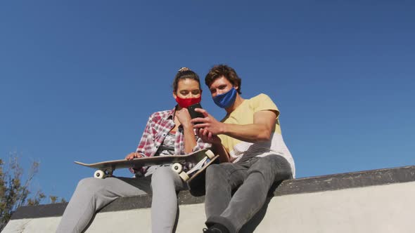 Caucasian woman and man friend wearing face mask, sitting and using smartphone